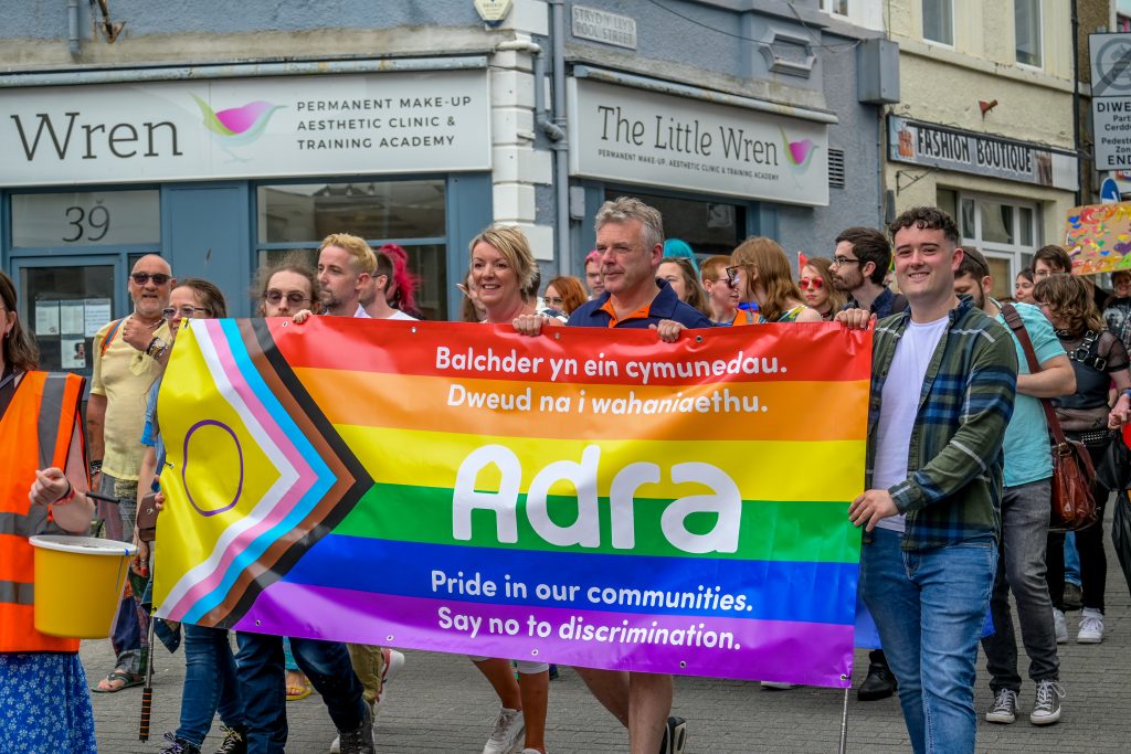 Staff Adra gyda banner Pride yn orymdaith Balchder Gogledd Cymru