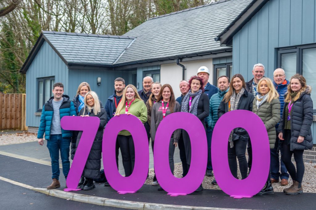 Group of people standing outside a bungalow with large 7,000 purple numbers