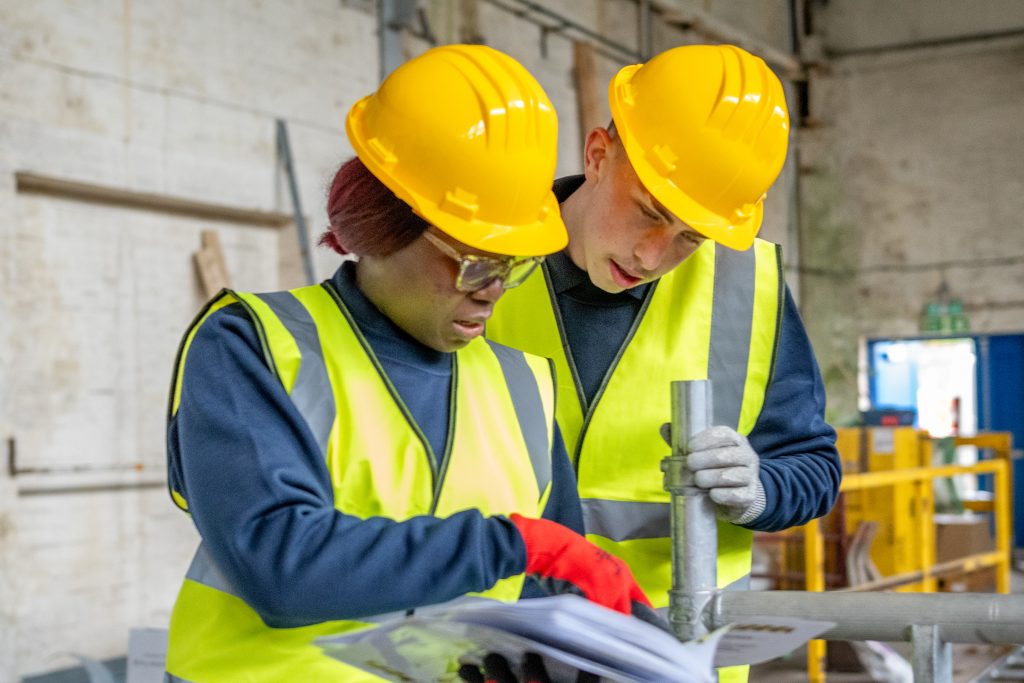 Photo of a woman and a man looking at instructions, wearing hi vis clothing and hard hat